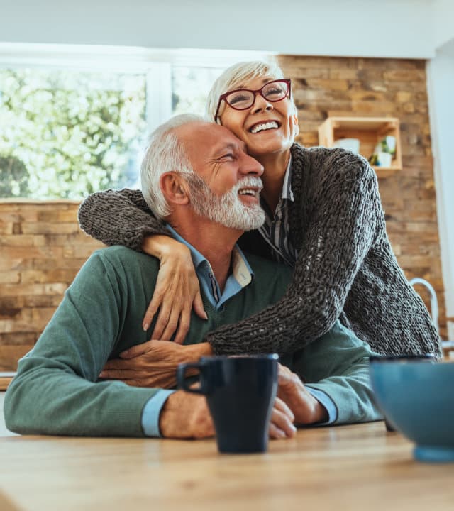 A happy senior couple embracing at a table with a mug, sharing a moment