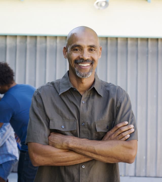 A smiling, middle-aged or senior bald Black man standing with his arms crossed.